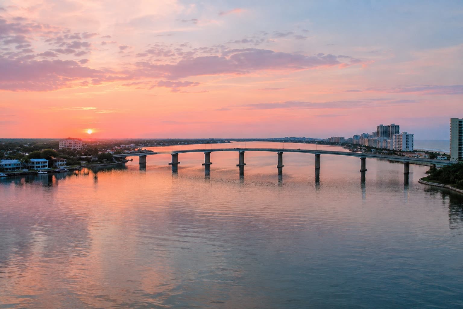 Aerial view of a curved bridge connecting two shorelines over calm water at sunset